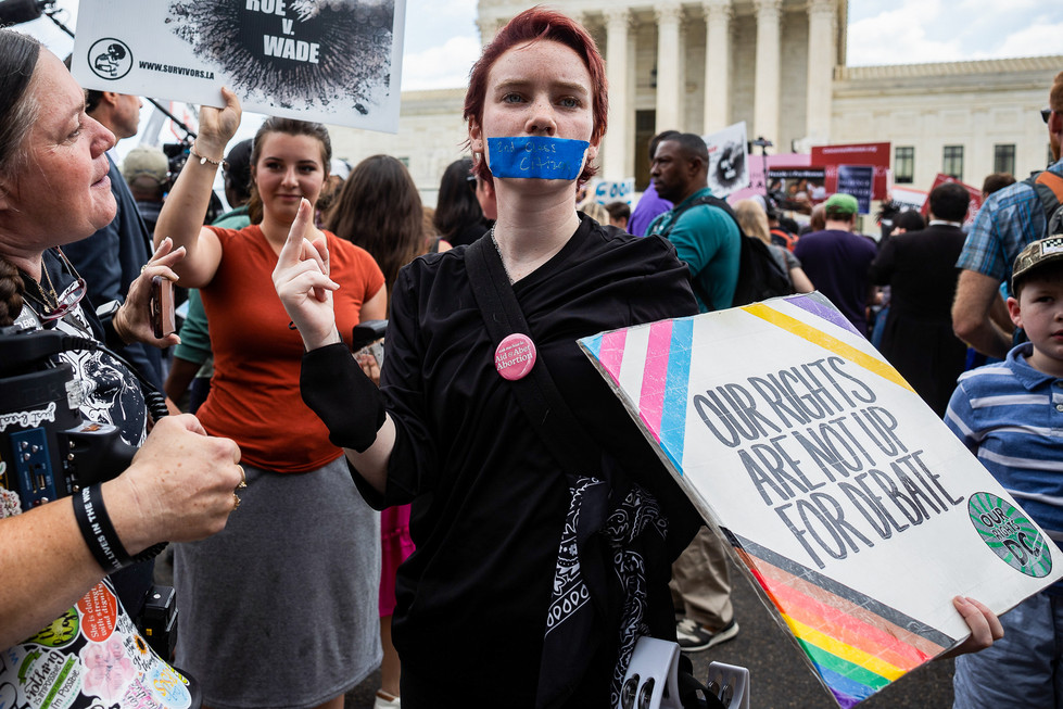 A person with their mouth taped holding up a sign outside the Supreme Court.