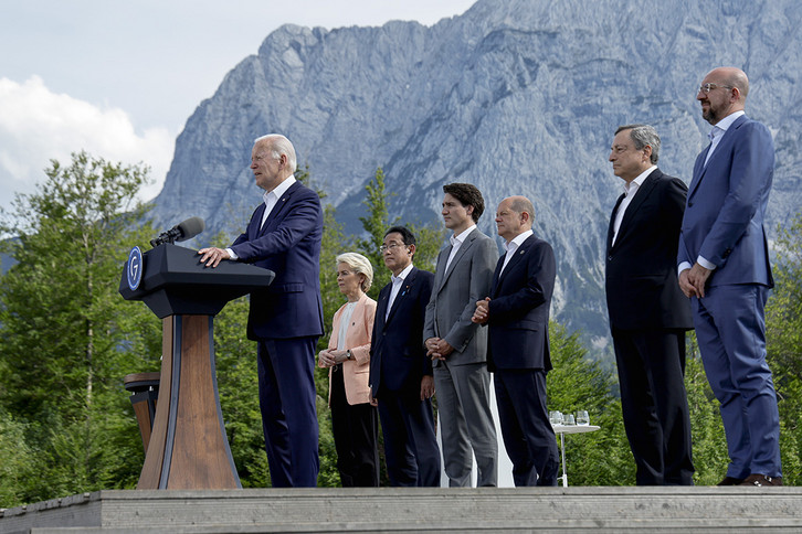 President Joe Biden speaks at a lectern as world leaders stand behind him.