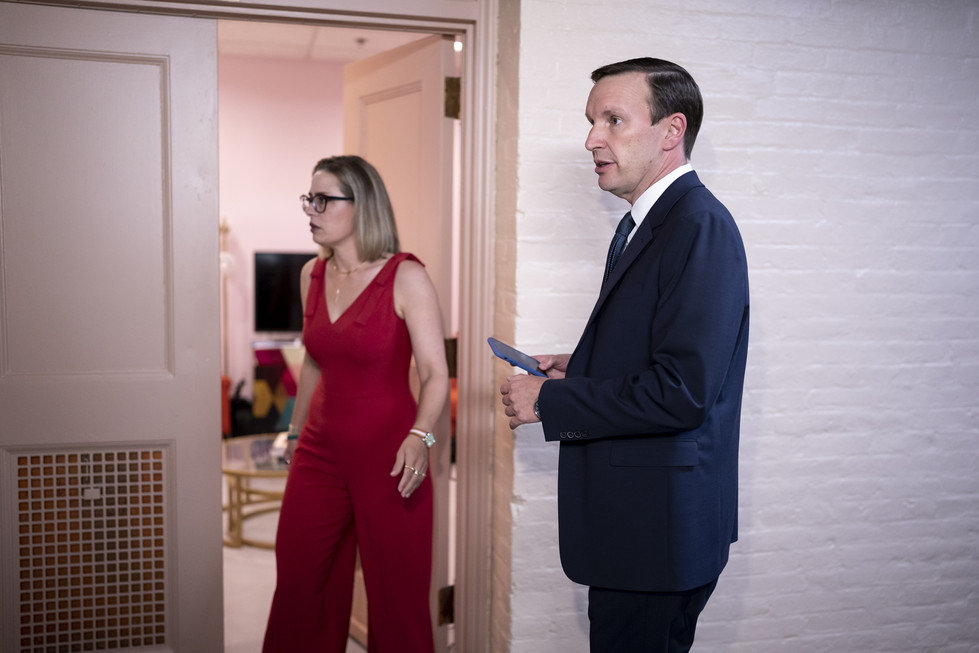 Kyrsten Sinema and Chris Murphy stand in a hallway.