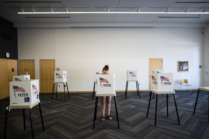A woman stands behind a voting booth.