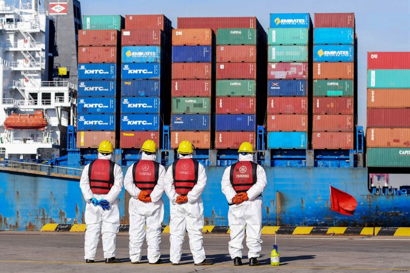 Employees watch a cargo ship at a port in China, which is experiencing an economic downturn.