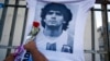 FILE - A man places a flower on a jersey with the face of the late football star Diego Maradona during a march to demand answers regarding his death in Buenos Aires, Argentina, March 10, 2021. 