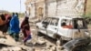 FILE - Women walk next to a destroyed house and car after an explosion set off by al-Shabab militants in Mogadishu, Somalia, Feb. 16, 2022. Al-Shabab has long been fighting to dislodge the central government. One of its most recent attacks occurred June 17, 2023, in Adado.