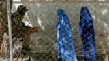 FILE - A Taliban fighter stands guard as two women enter the government passport office, in Kabul, Afghanistan, April 27, 2022. Afghanistan's Taliban leadership has ordered all Afghan women to wear the all-covering burqa in public.