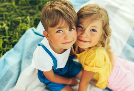 Outdoors close up portrait of smiling two children playing on the blanket outdoors. Little boy and cute little girl bonding and relaxing in the park. Kids having fun on sunlight. Sister and brother