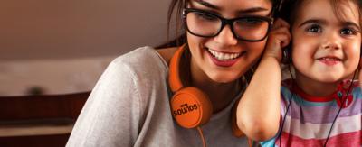 A mother and her daughter listening to sounds through headphones. The mother has orange headphones around her neck with the BBC Sounds logo.