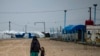 FILE - This file photo taken on March 4, 2021 shows a woman holds a child's hand as they stand in the rain at Camp Roj, where relatives of people suspected of belonging to the Islamic State (IS) group are held, near al-Malikiyah (Derik) in Syria's northea