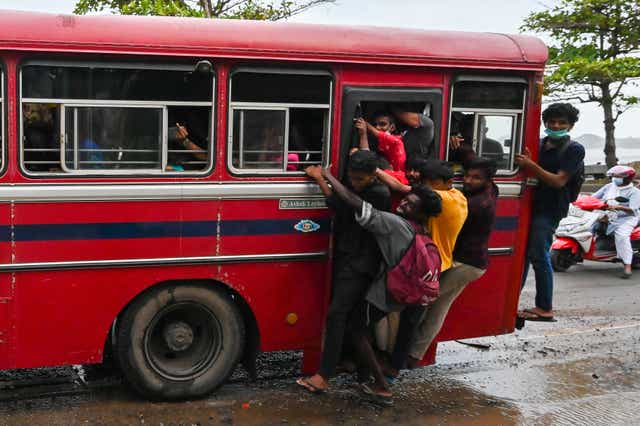 <p>Passengers hang from a door of a crowded public transport bus in Galle</p>