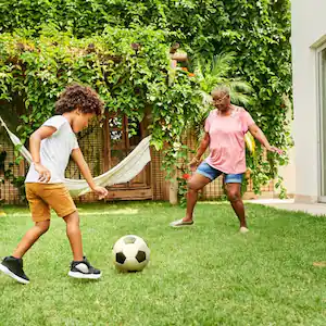 A grandson playing soccer with his grandma in the backyard