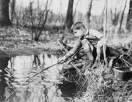 Boy leaning over water fishing with a home-made fishing pole.