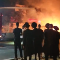 A group of Haredi men watch as a firetruck works to extinguish a fire caused by riots at the Bar Ilan Junction in Jerusalem, July 7, 2022. (Screenshot/Twitter)