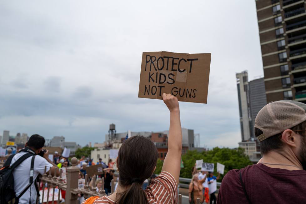 A person holds up a &quot;Protect Our Kids Not Guns&quot; sign. 