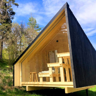 A small wooden house with one side made of glass, with wooden benches visible inside.