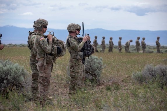 Forward observers stand outside the landing  zone as two UH-60 helicopters land to take these soldiers out to an observation point to train on marking targets for artillery during Western Strike 22, June 9, 2022