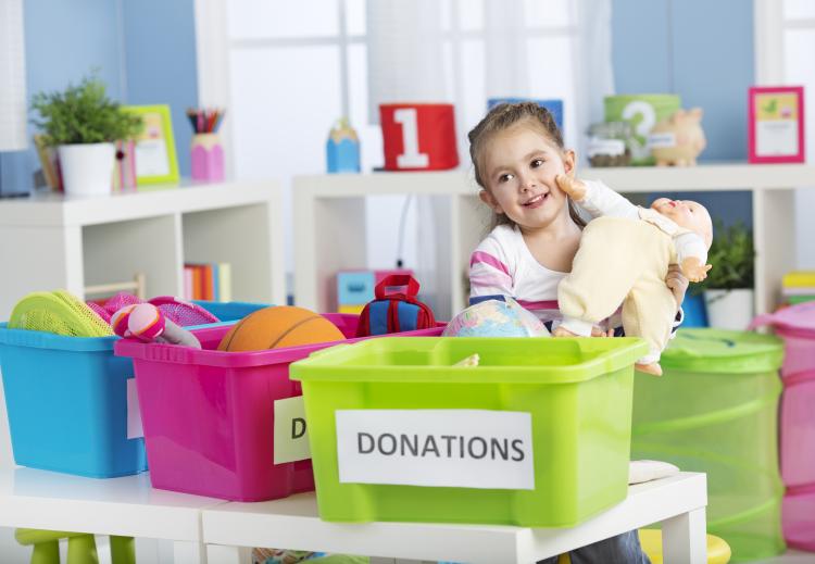 Little girl cleaning out her toys and donating a doll.