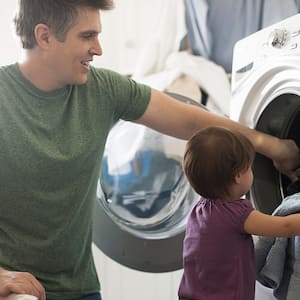 Toddler helps dad put laundry into dryer