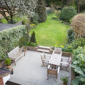 overhead view of concrete patio with lawn furniture next to lush garden flowers and plants and grassy yard