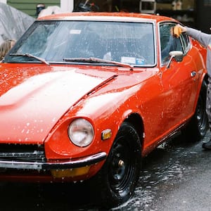 A little boy with his father wash their red vintage car in the driveway of their home