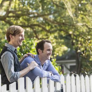 A smiling couple leans against a white picket fence