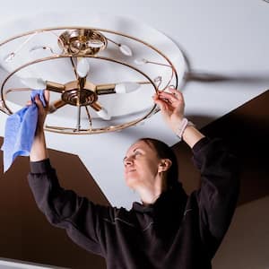  A woman getting rid of cobwebs from a light fixture