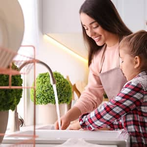 Mother and daughter wash dishes together in kitchen sink