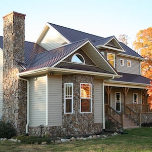 view of house with tan siding, stone accents, and brown metal roof