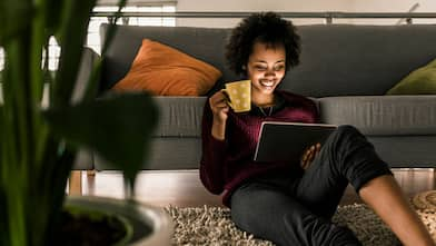 A smiling woman drinking coffee while browsing her laptop