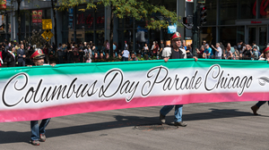 People walking in a parade with a Columbus Day banner.