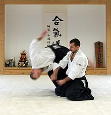 A man kneeling throws another man from a standing position; both are wearing robes