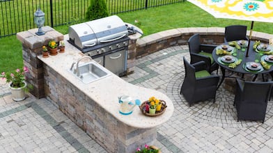 An outdoor kitchen and a dining table in a paved patio