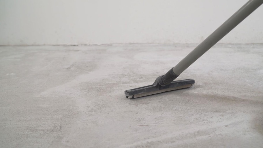 A worker is cleaning the concrete floor with a vacuum cleaner.