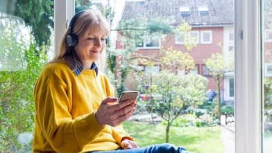 Woman wearing headphones sitting by an open window