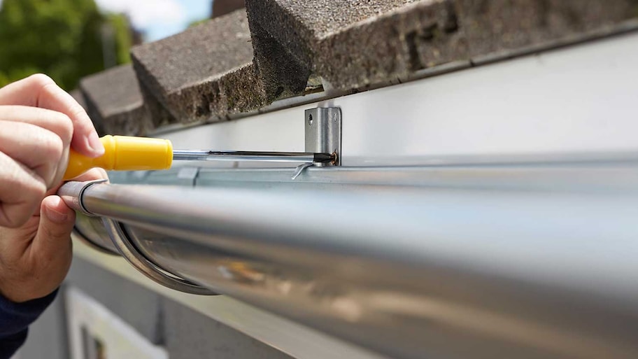 Person securing gutter on house