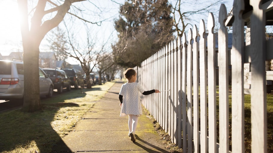 Girl walking next to white picket fence