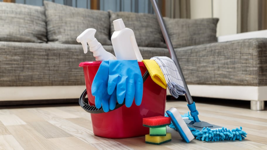 bucket of cleaning supplies sits on light wood floor in front of grey couch