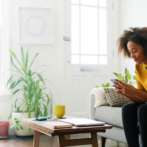 A woman using her smartphone on her living room’s sofa