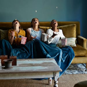 Friends sitting under a blanket catching popcorn with their mouth