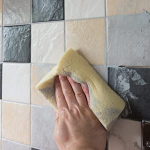 A hand in glove wiping of grout from new tiles