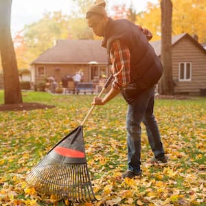 A young man raking leaves in his backyard in autumn