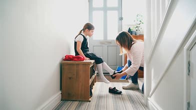 Mom puts daughters shoes on in entryway