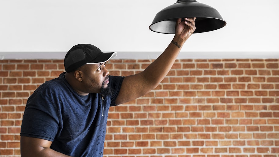 man replaces light bulb in pendant light fixture