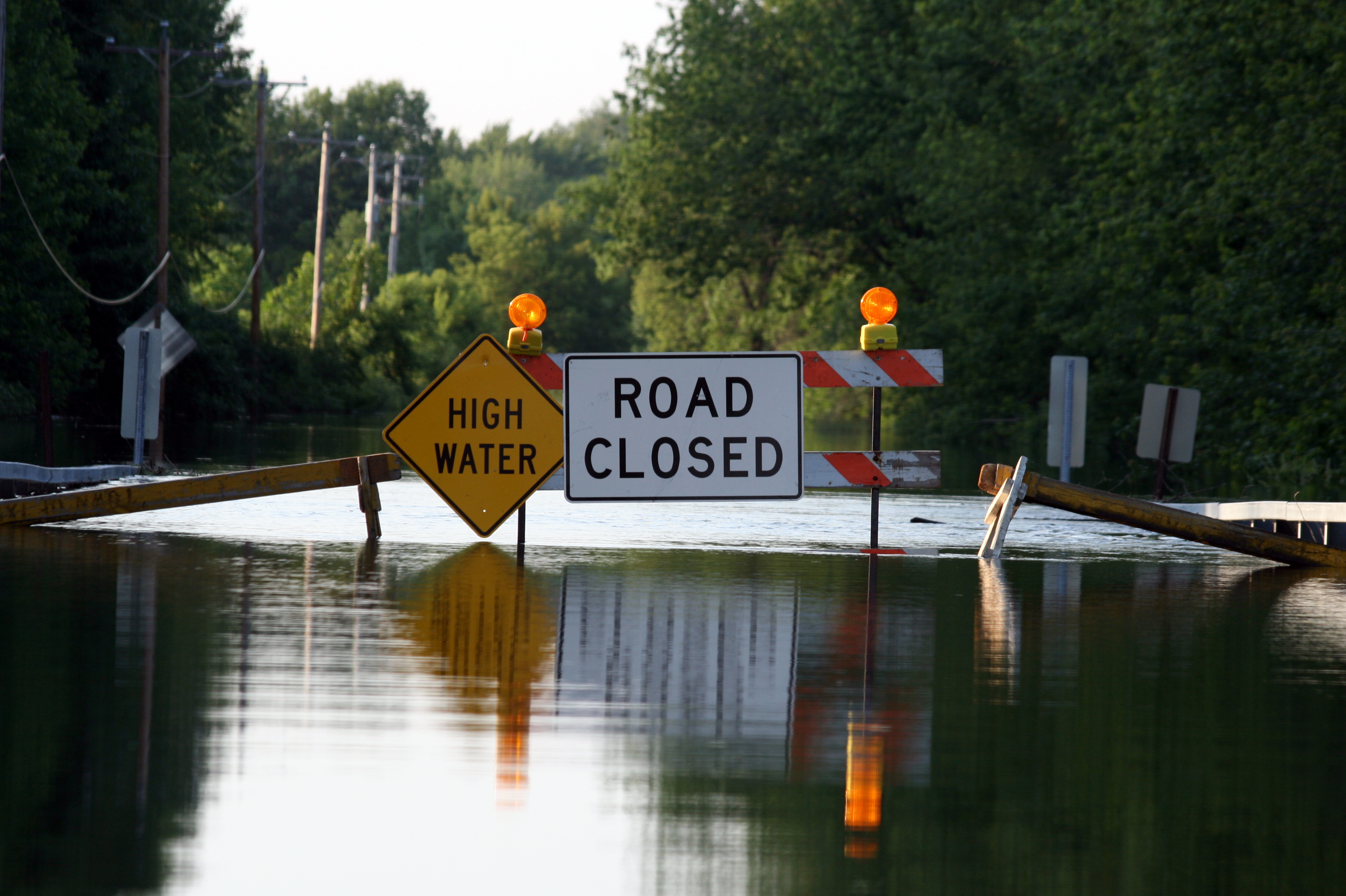 A flooded road with a sign that says, “High Water. Road Closed.” 