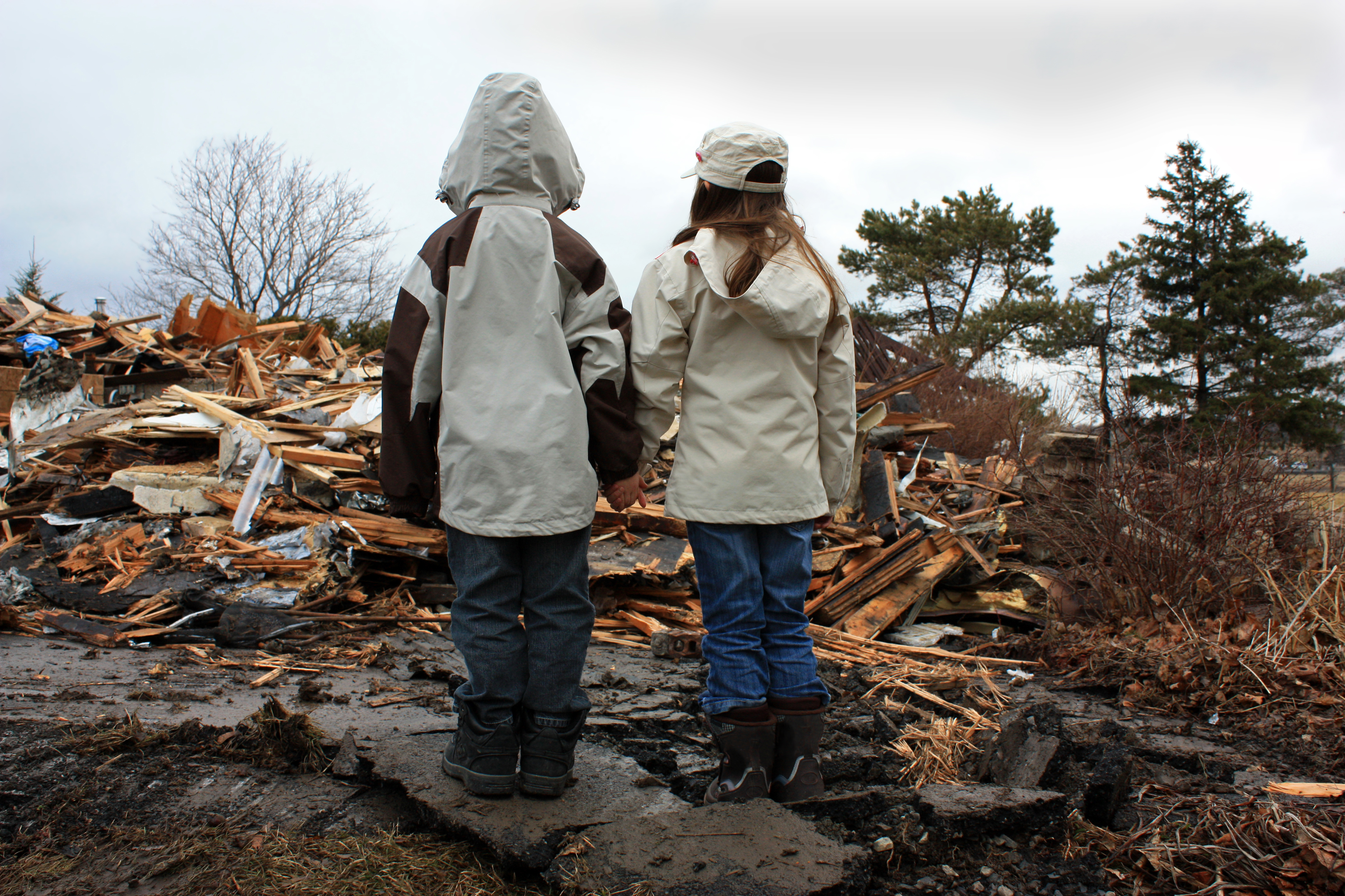 Two children standing outside and looking at a pile of rubble after a natural disaster 