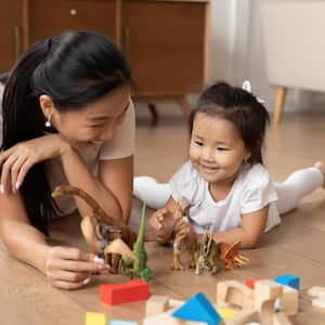 Mom plays dinosaurs with toddler laying on floor