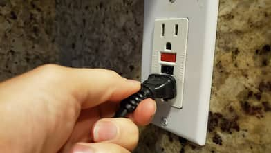 human hand of a man plugging an electrical cord into a GFCI electrical outlet