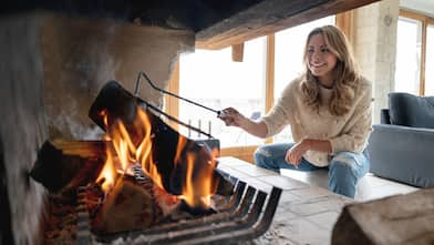 Woman wearing a sweater is stoking a fire in a fireplace