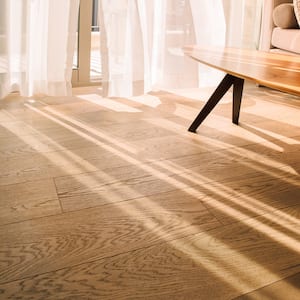 closeup of wood flooring with window and tulle curtain letting light shine across it and part of coffee table in corner