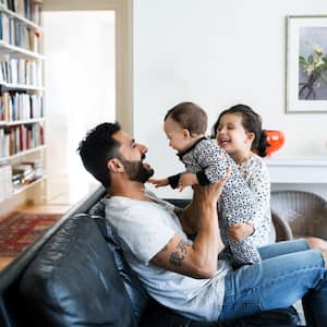 Father and daughter playing with baby girl on sofa at home