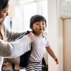 Mother helping toddler put on sweater in house