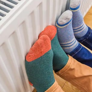 two sets of feet in colorful socks pushed against a white gas radiator
